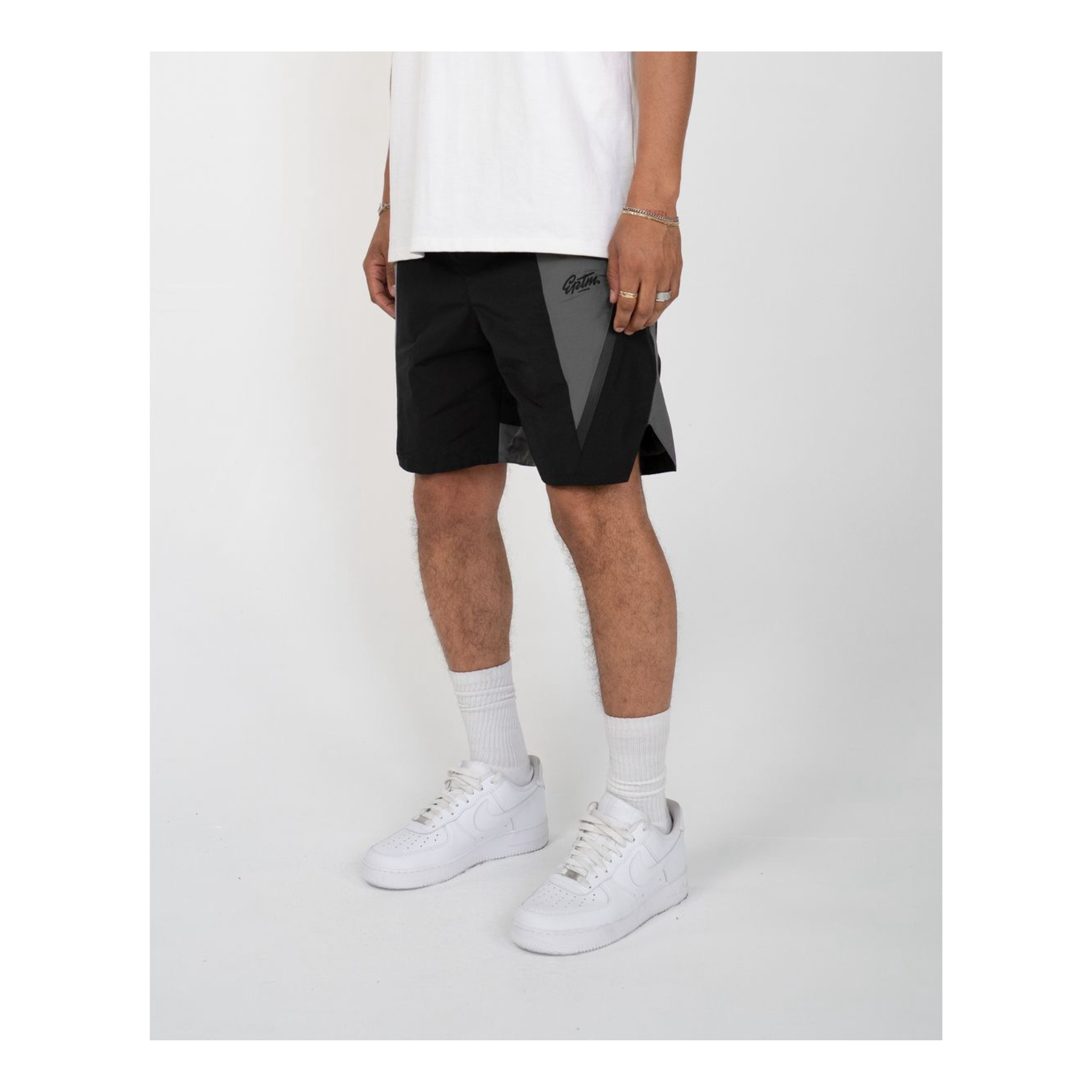 Person wearing black and grey shorts with white sneakers with a grey background.